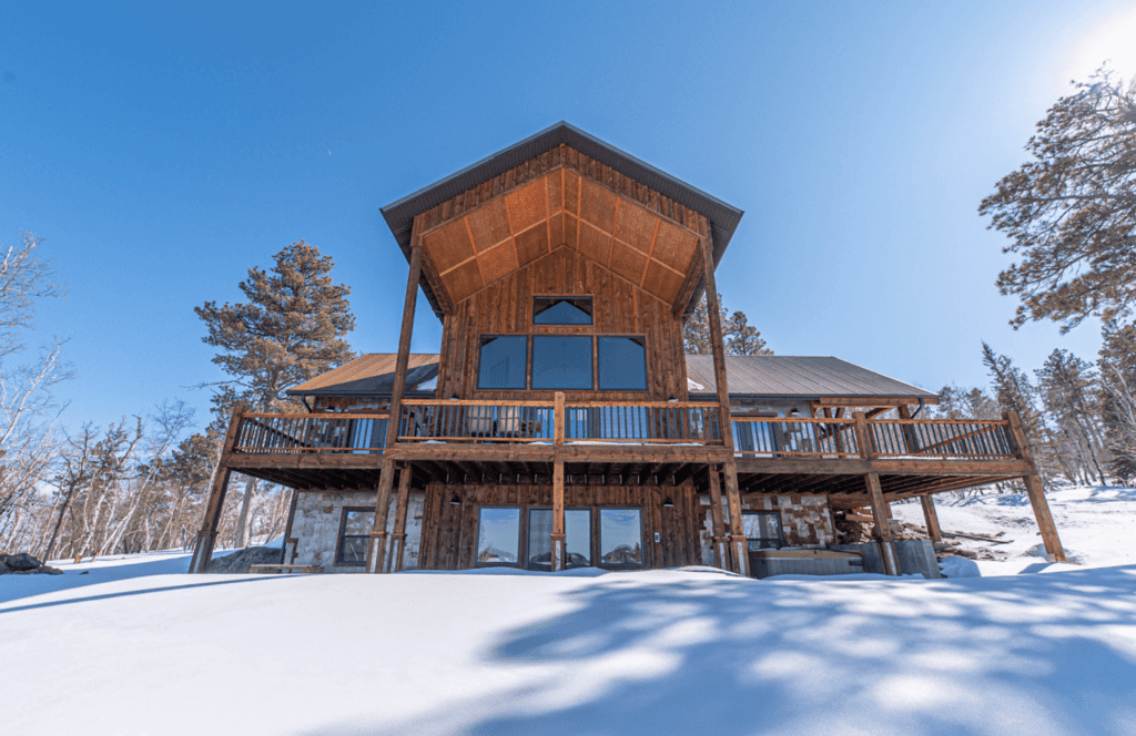 Exterior of Among The Pines custom home with massive deck surrounded by pine trees in the Black Hills. The home was built by Legacy Custom Homes and Design in Spearfish, SD.