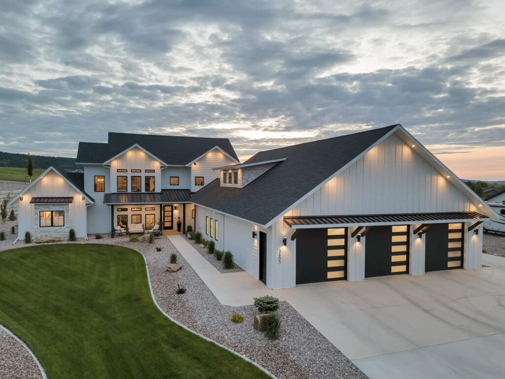 Modern two-story custom home with white board-and-batten siding, large black-trimmed windows, and a three-car garage, built by Legacy Custom Homes & Design in the Top Shelf Development in Spearfish, SD.