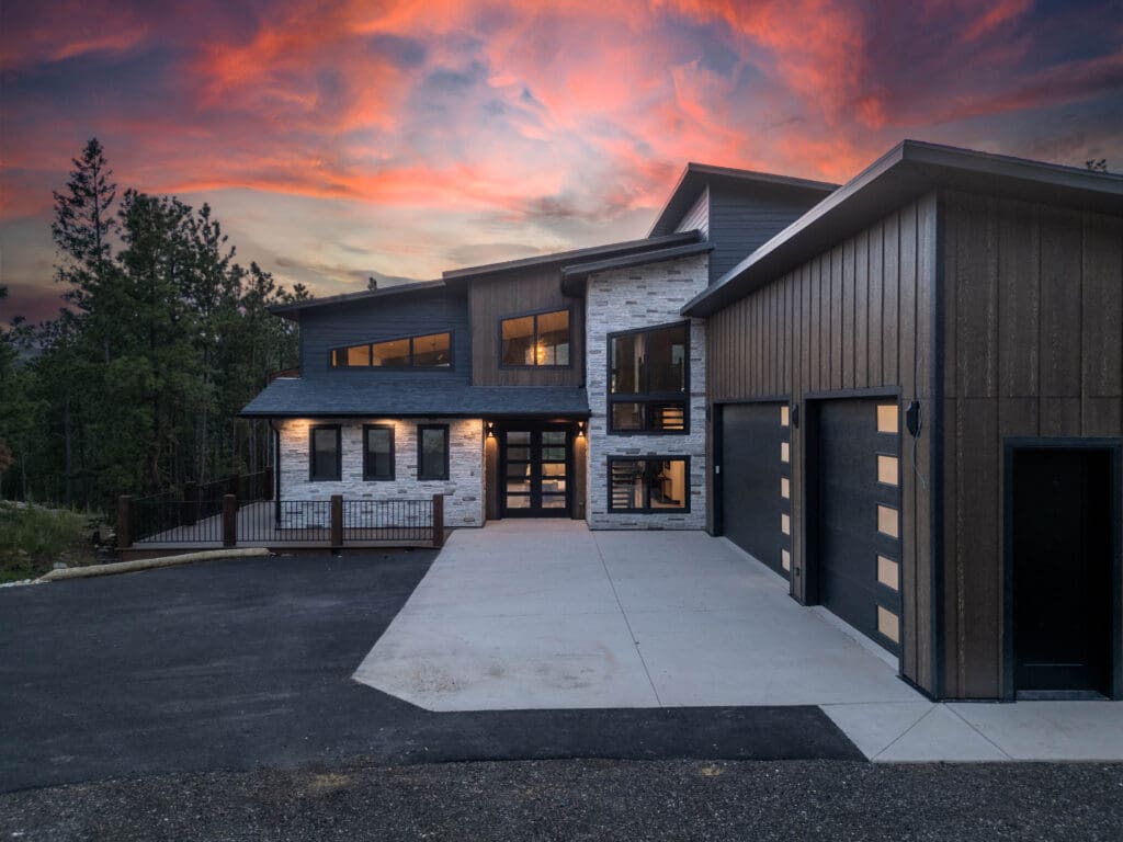 Modern custom home in Powder House Pass built by Legacy Custom Homes & Design featuring mountain architecture and three-car garage at sunset.