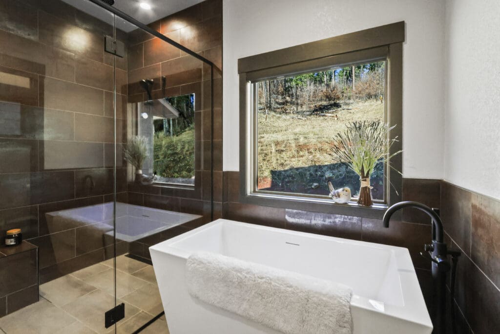 Luxury custom bathroom built by Legacy Custom Homes & Design, featuring a freestanding soaking tub, walk-in tile shower, custom glass enclosure, modern fixtures, and Black Hills views.